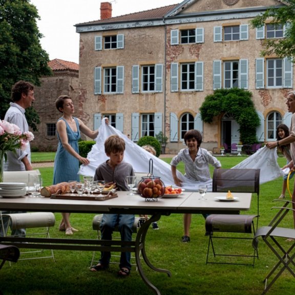 Fermob Romane extendable outdoor table in Nutmeg colour with a family in front of French chateau