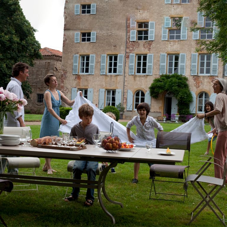 Fermob Romane extendable outdoor table in Nutmeg colour with a family in front of French chateau