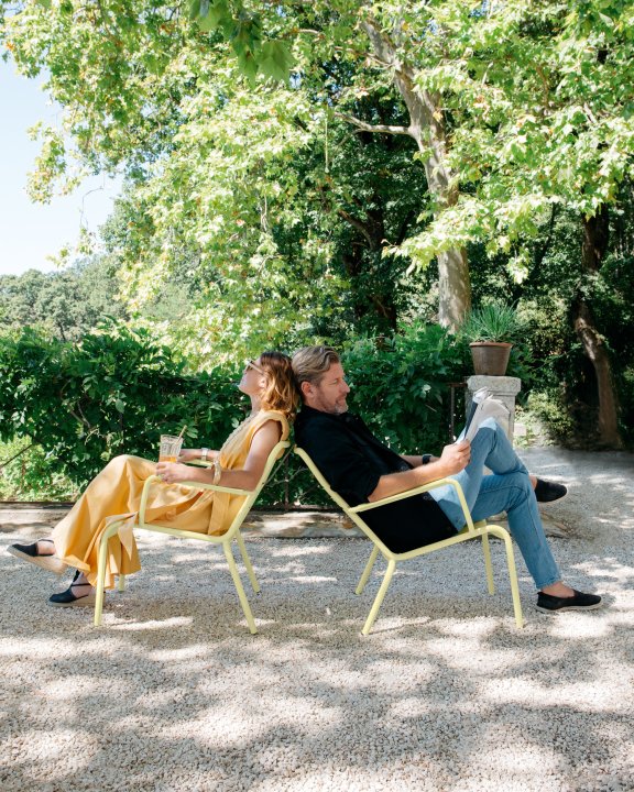A couple relax outdoors on Fermobs Luxembourg armchairs