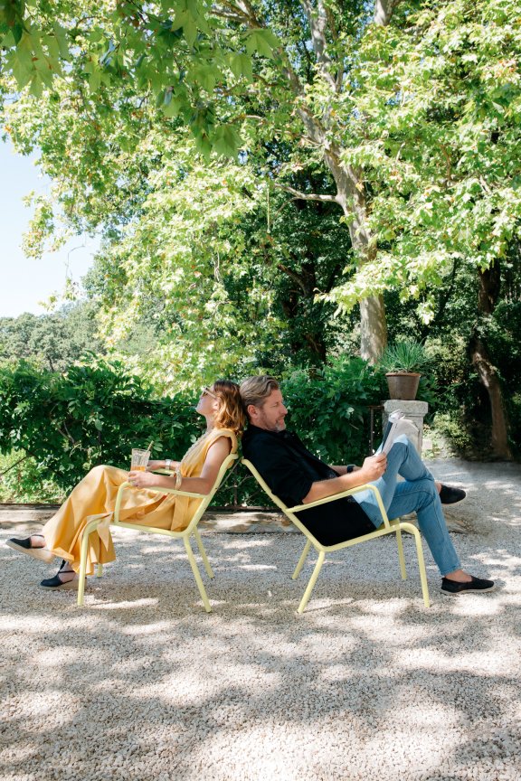 A couple relax outdoors on Fermobs Luxembourg armchairs