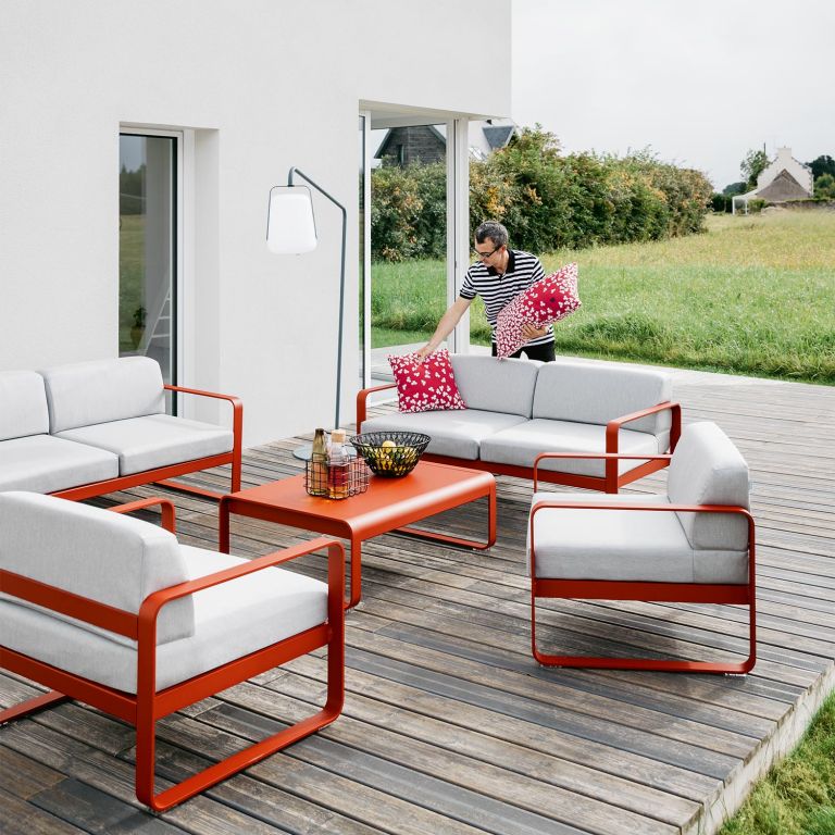 Man places cushion on Fermob Bellevie Two Seater Outdoor Sofa in Chilli colour on a residential house deck