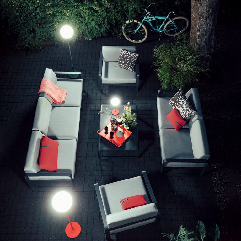 Fermob Bellevie sofa setting in Anthracite on paved courtyard at night lit by Fermob Mooon! outdoor lamp